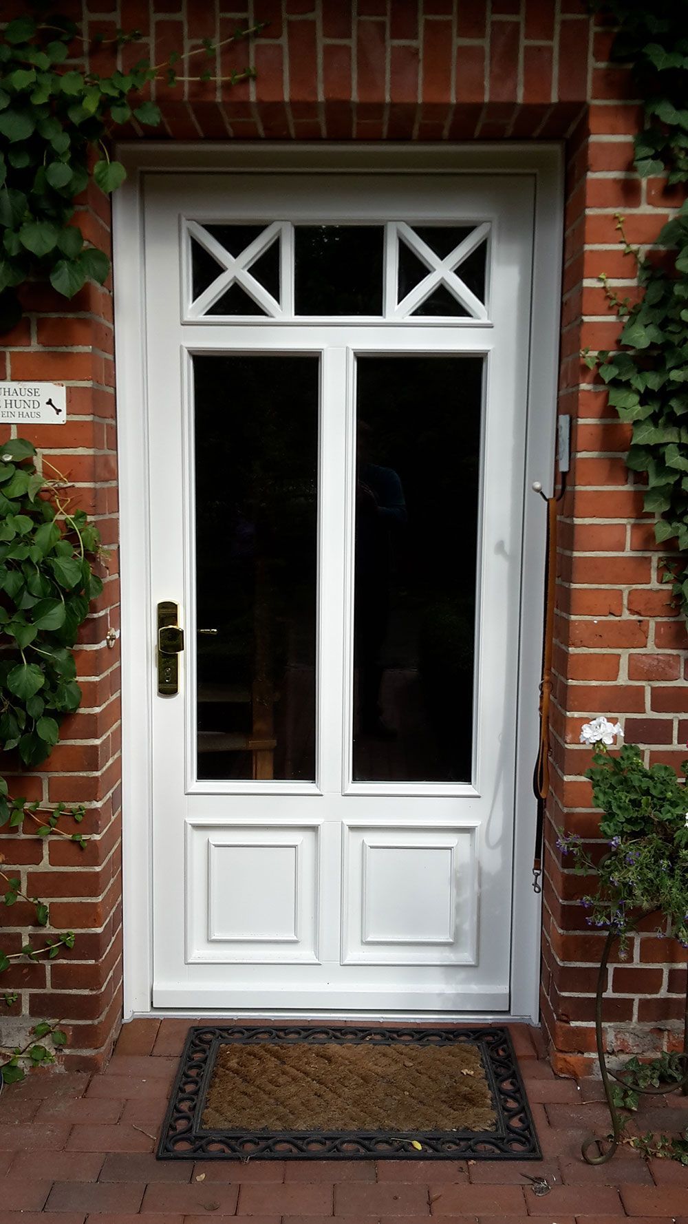 Eine weiße Tür mit einer schwarzen Matte vor einem Backsteingebäude.
