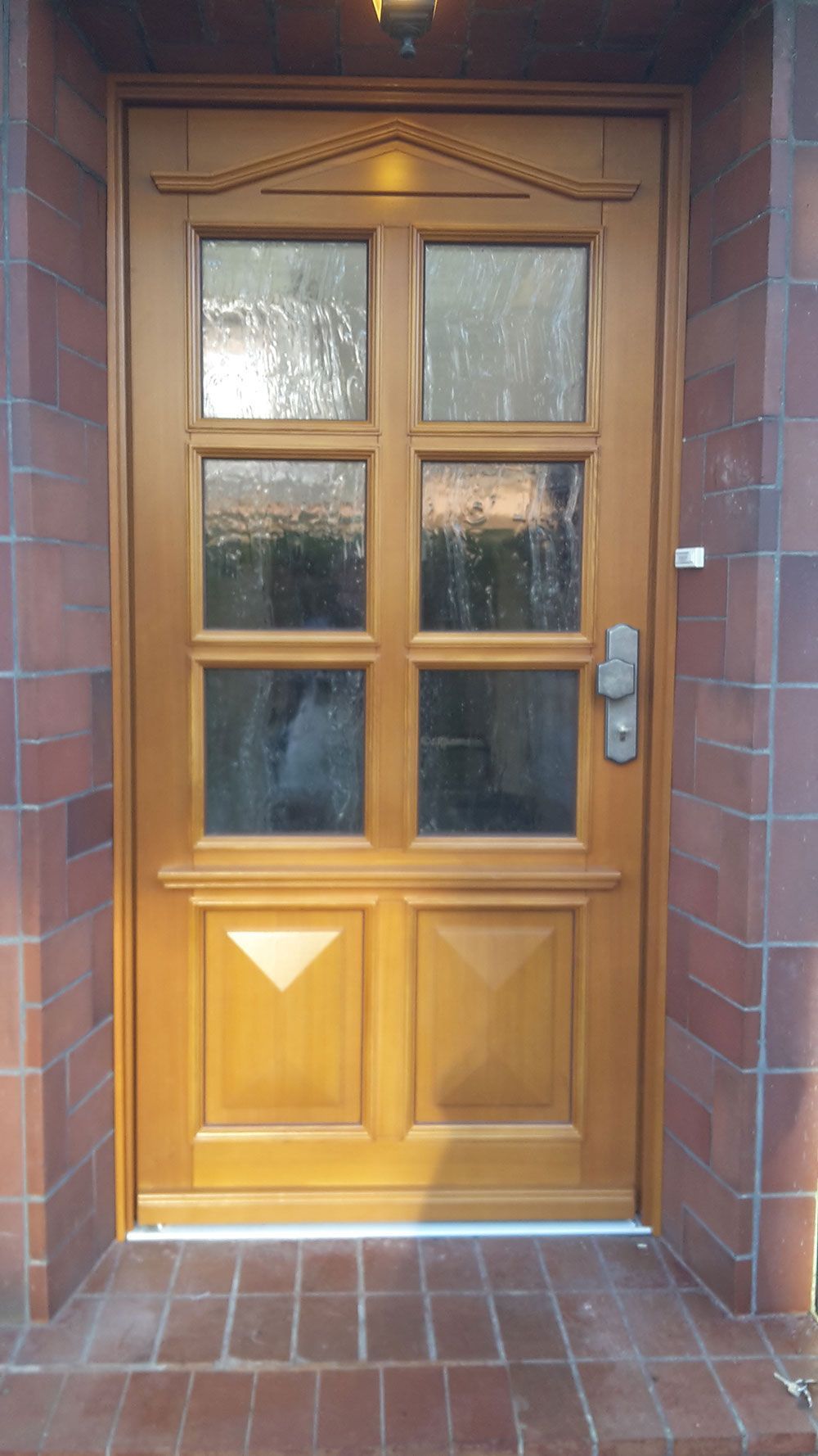 In einer Backsteinmauer sitzt eine Holztür mit vier Fenstern.