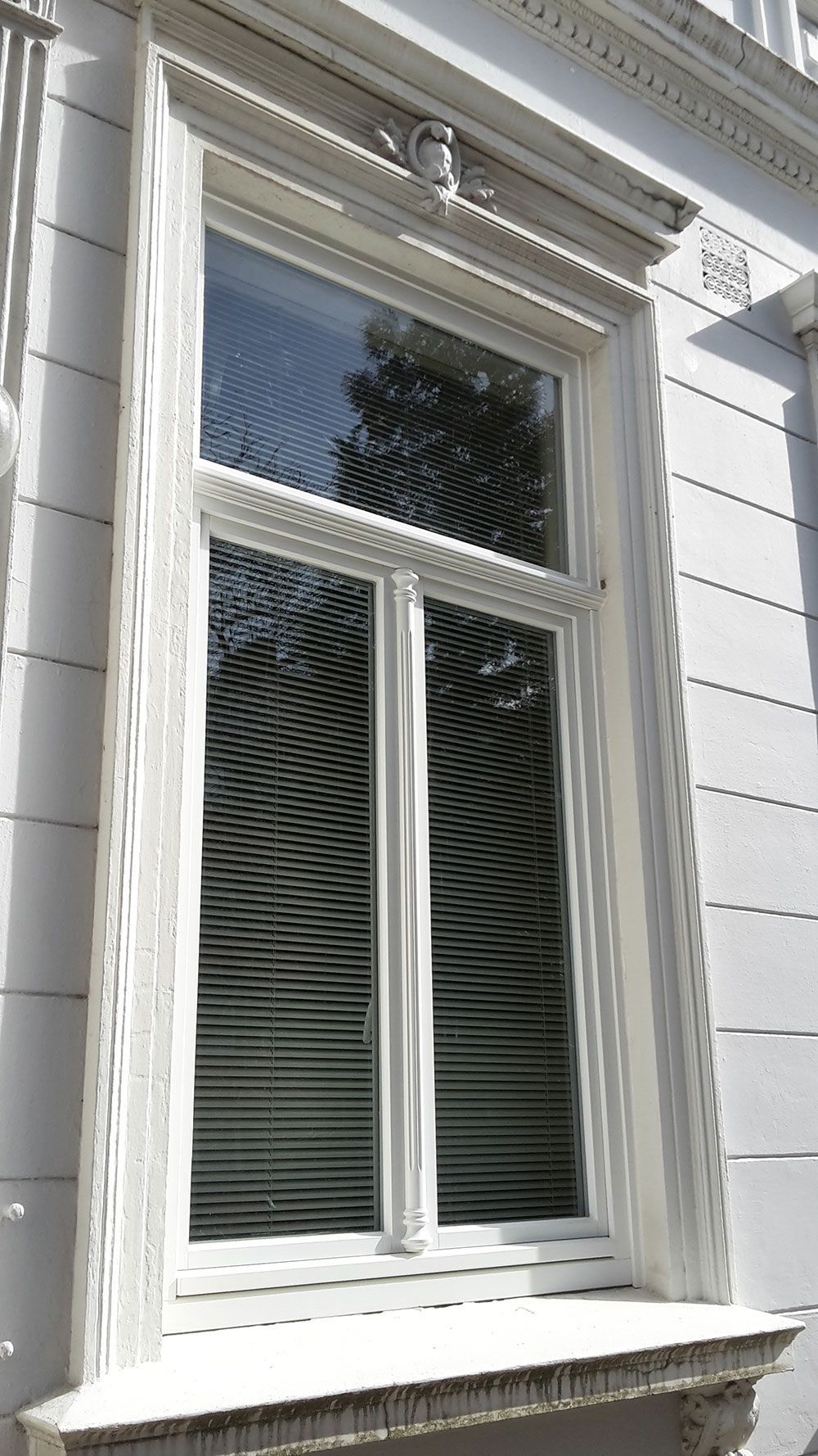 An der Seite eines Gebäudes befindet sich ein weißes Fenster mit Jalousien.