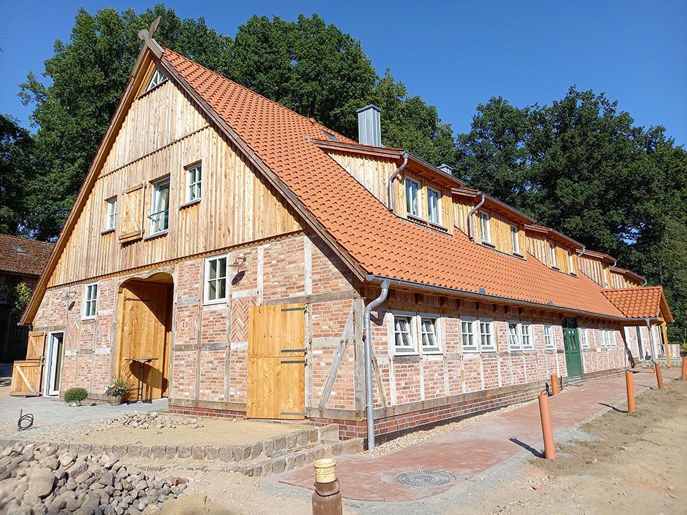 Ein großes Holzhaus mit einem roten Ziegeldach ist von Bäumen umgeben.