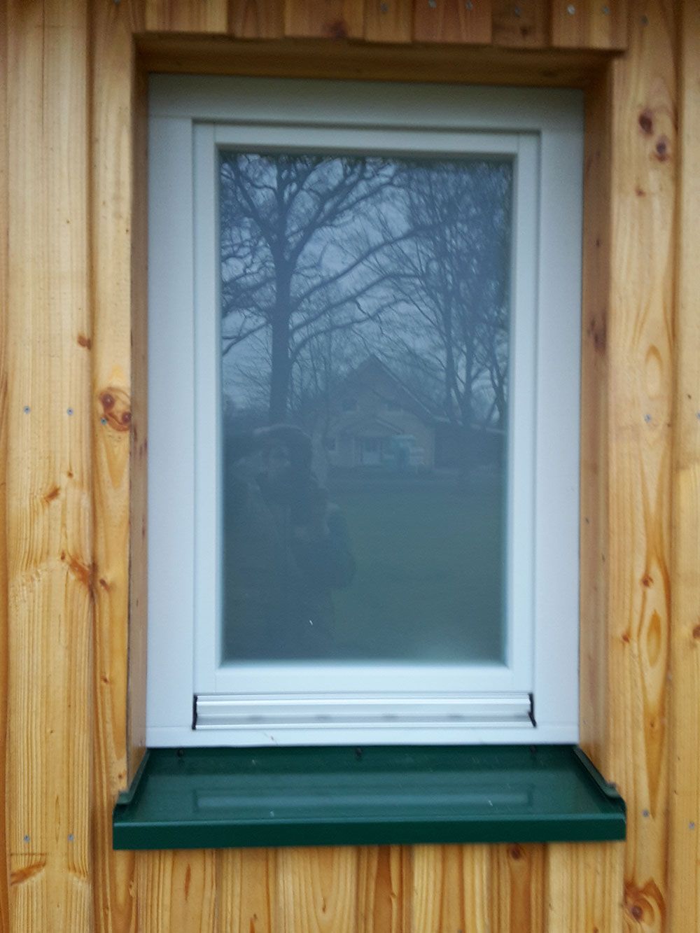 An einer Holzwand befindet sich ein weißes Fenster mit grüner Fensterbank.