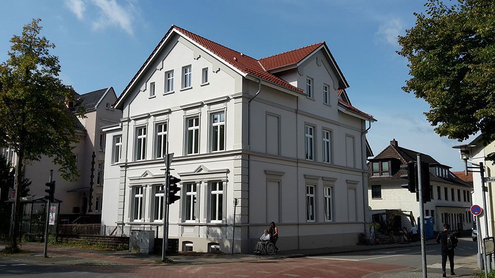 An einer Straßenecke steht ein großes weißes Gebäude mit rotem Dach.