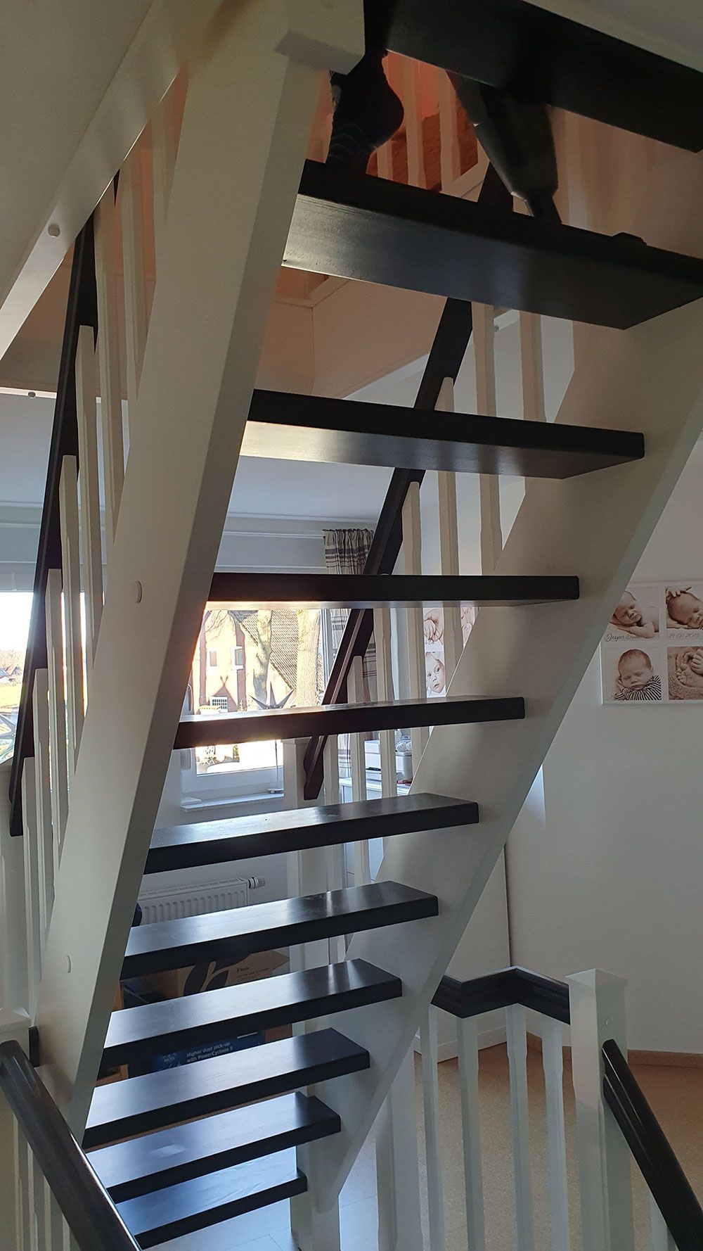 Eine Holztreppe mit schwarzen Stufen und weißem Geländer in einem Haus.
