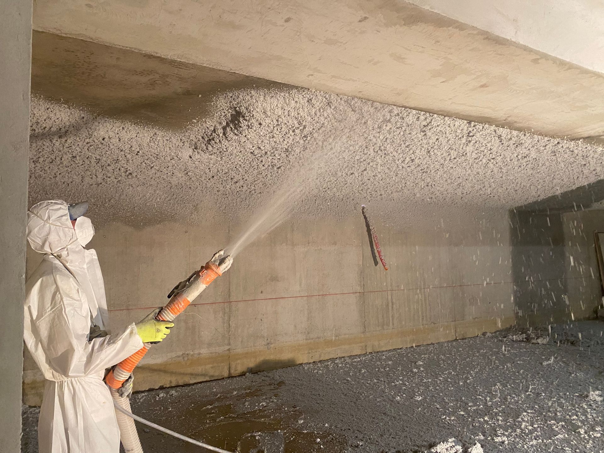 Une personne en combinaison de protection pulvérise de l'isolant dans un grenier.