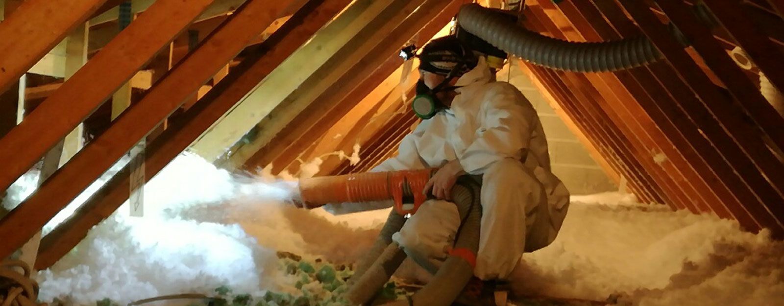 Personne installant de l'isolant dans un grenier, portant un équipement de protection. Isolant blanc projeté.