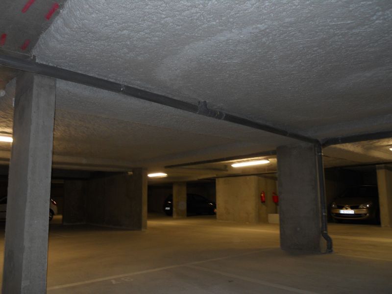 Parking souterrain avec piliers et plafond en béton, éclairage ambiant et voitures garées.