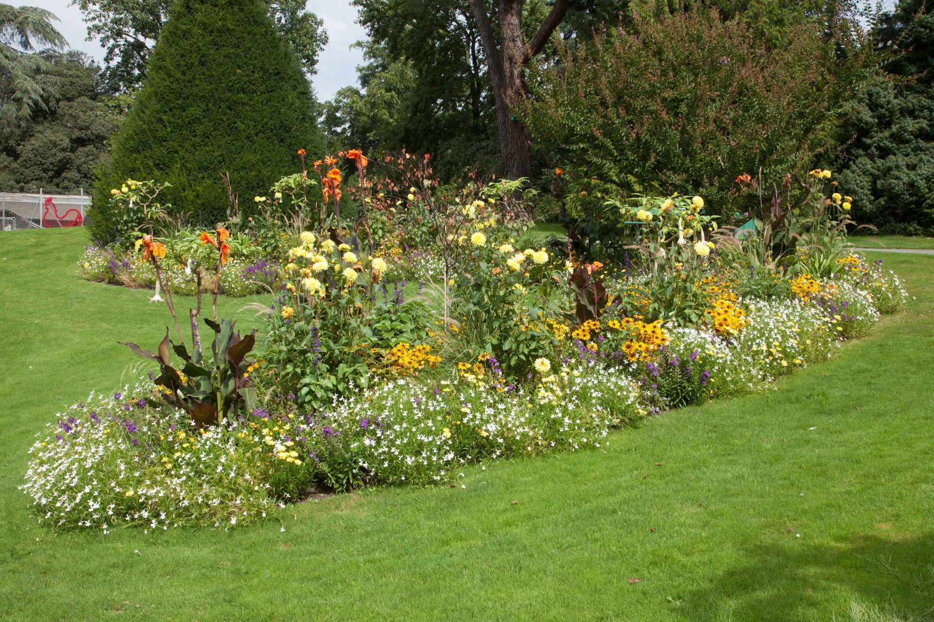 Parterre de fleurs aux teintes jaunes et orange dans une pelouse verdoyante de parc.