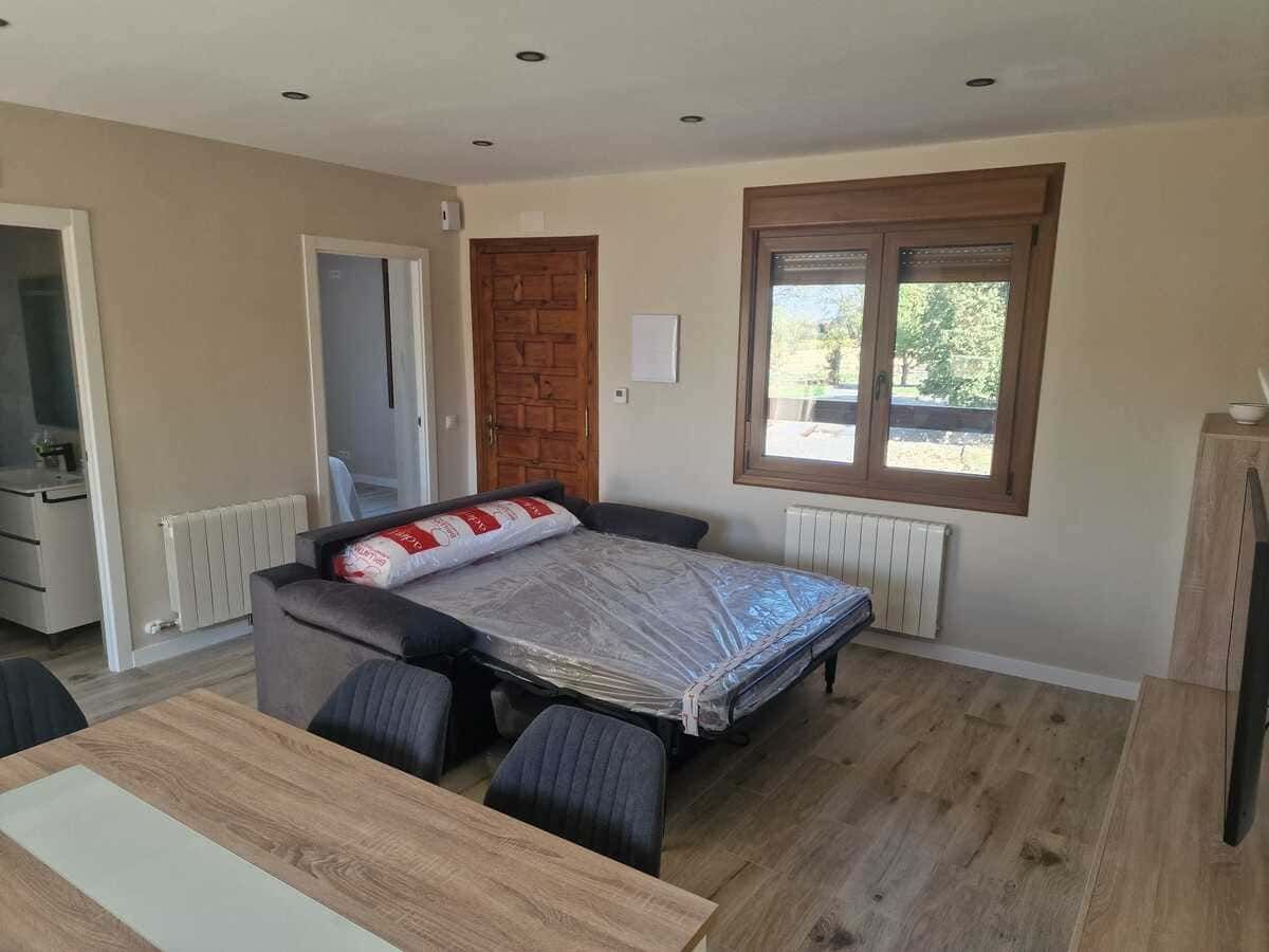 Dormitorio pequeño con una cama sin hacer, un escritorio de madera, una silla, una ventana y una puerta que da a un pasillo.