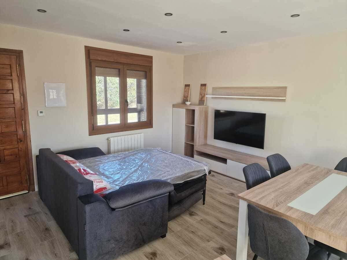 Sala de estar con sofá, televisor y muebles de madera, iluminada por una ventana y luces de techo