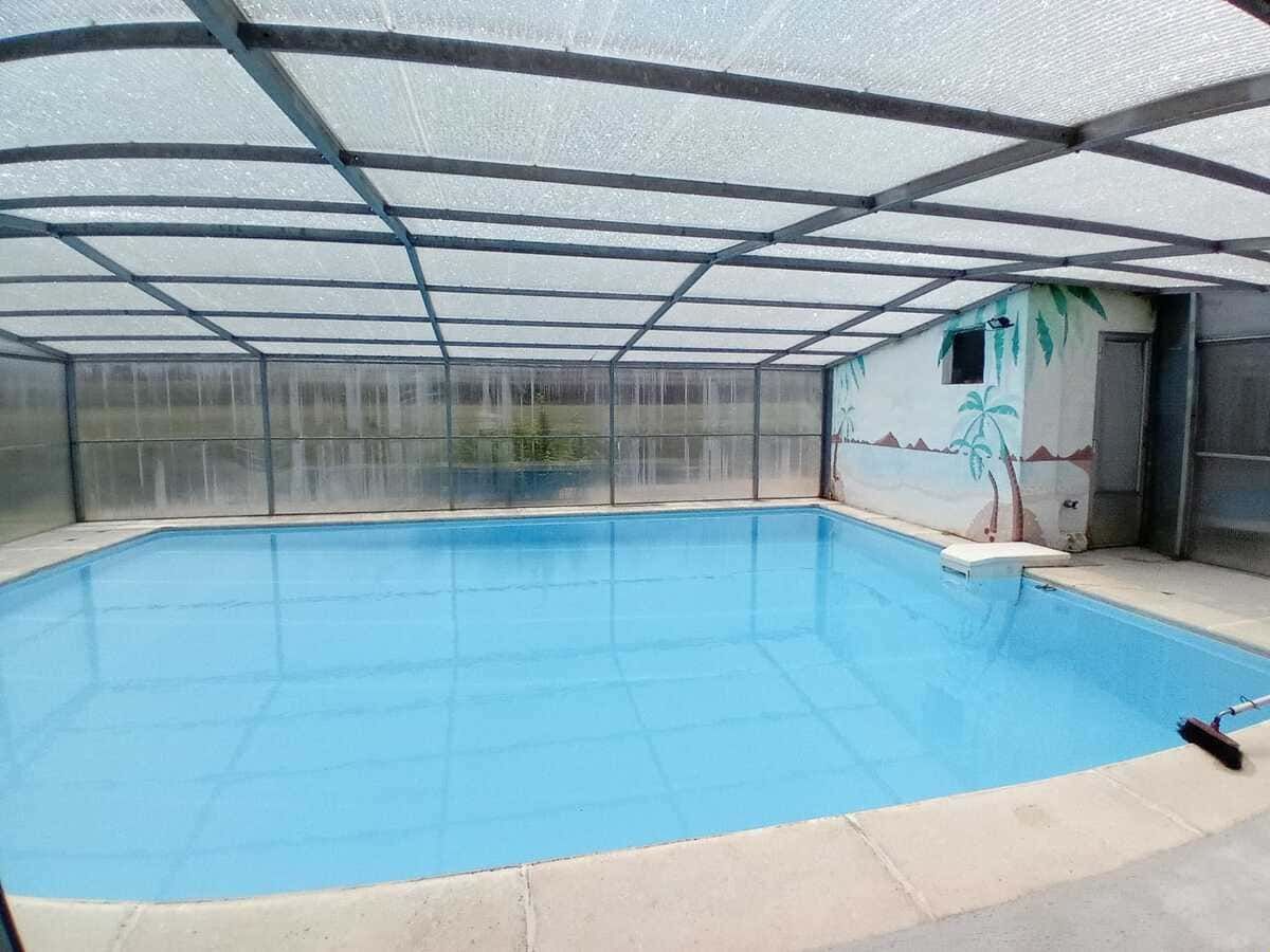 Piscina cubierta vacía, con agua azul, cerramiento con mosquitera y terraza de hormigón.