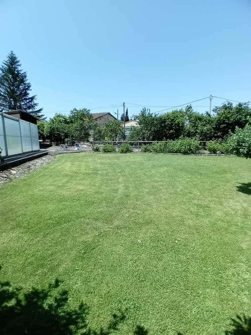 Casa rústica de piedra de dos plantas, con tejado de tejas rojas, balcón y jardín en un soleado paisaje rural