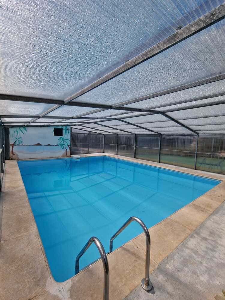 Piscina exterior cubierta, con agua azul, escalera metálica y una cubierta de malla encima.