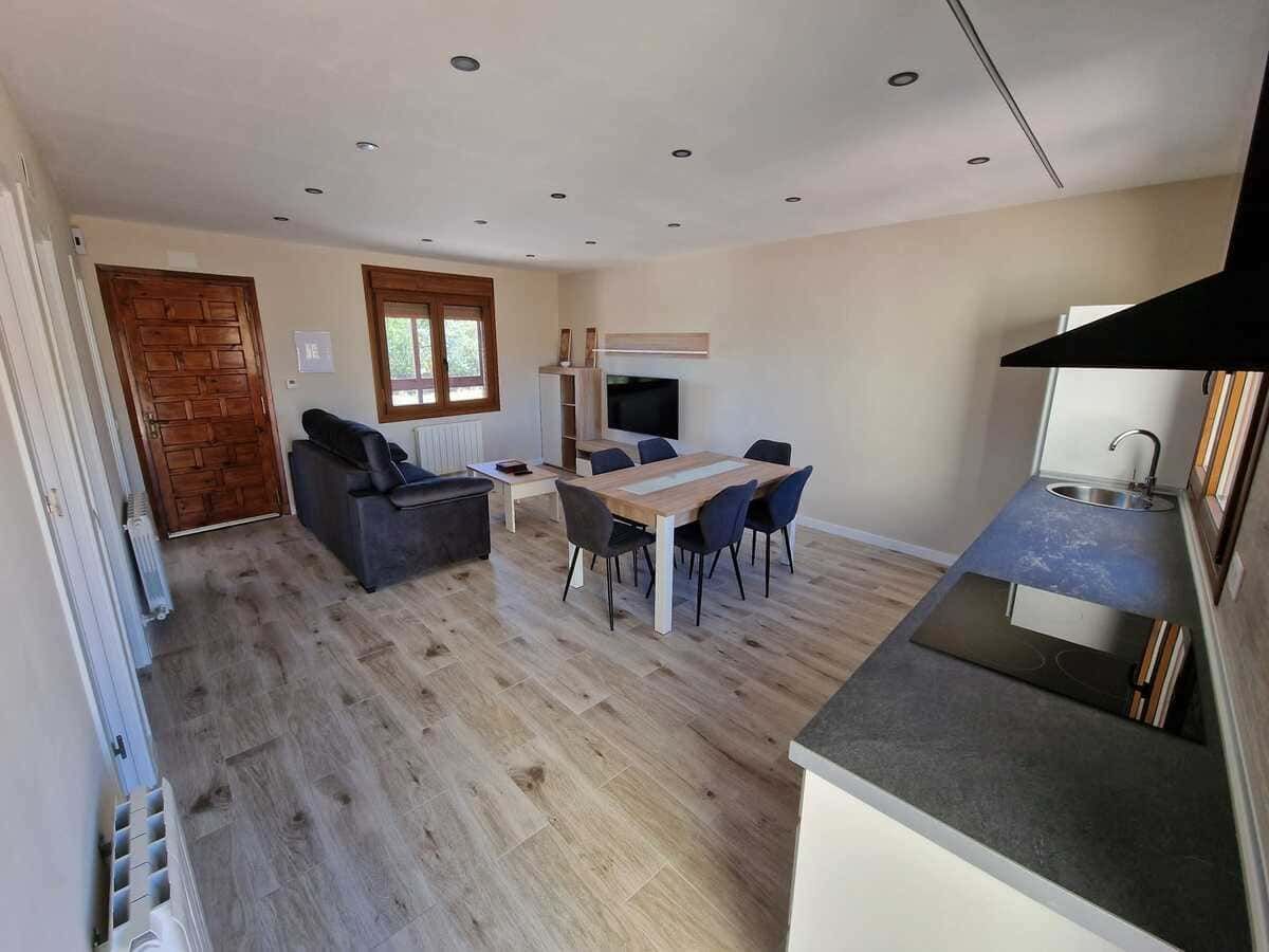 Salón de concepto abierto con sofá gris, mesa de comedor, barra de cocina y suelo de madera