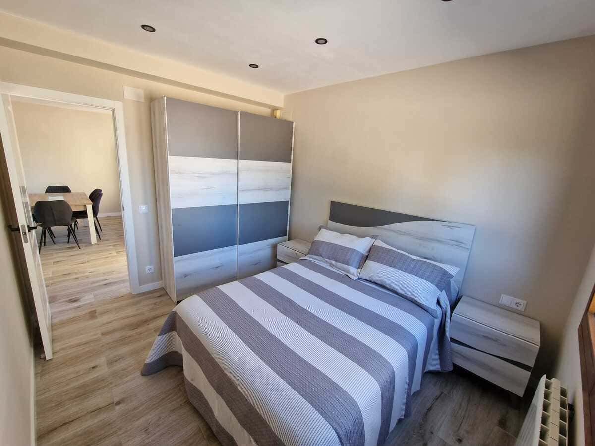 Dormitorio luminoso con una cama, ropa de cama a rayas, un armario y puertas de armario con espejo