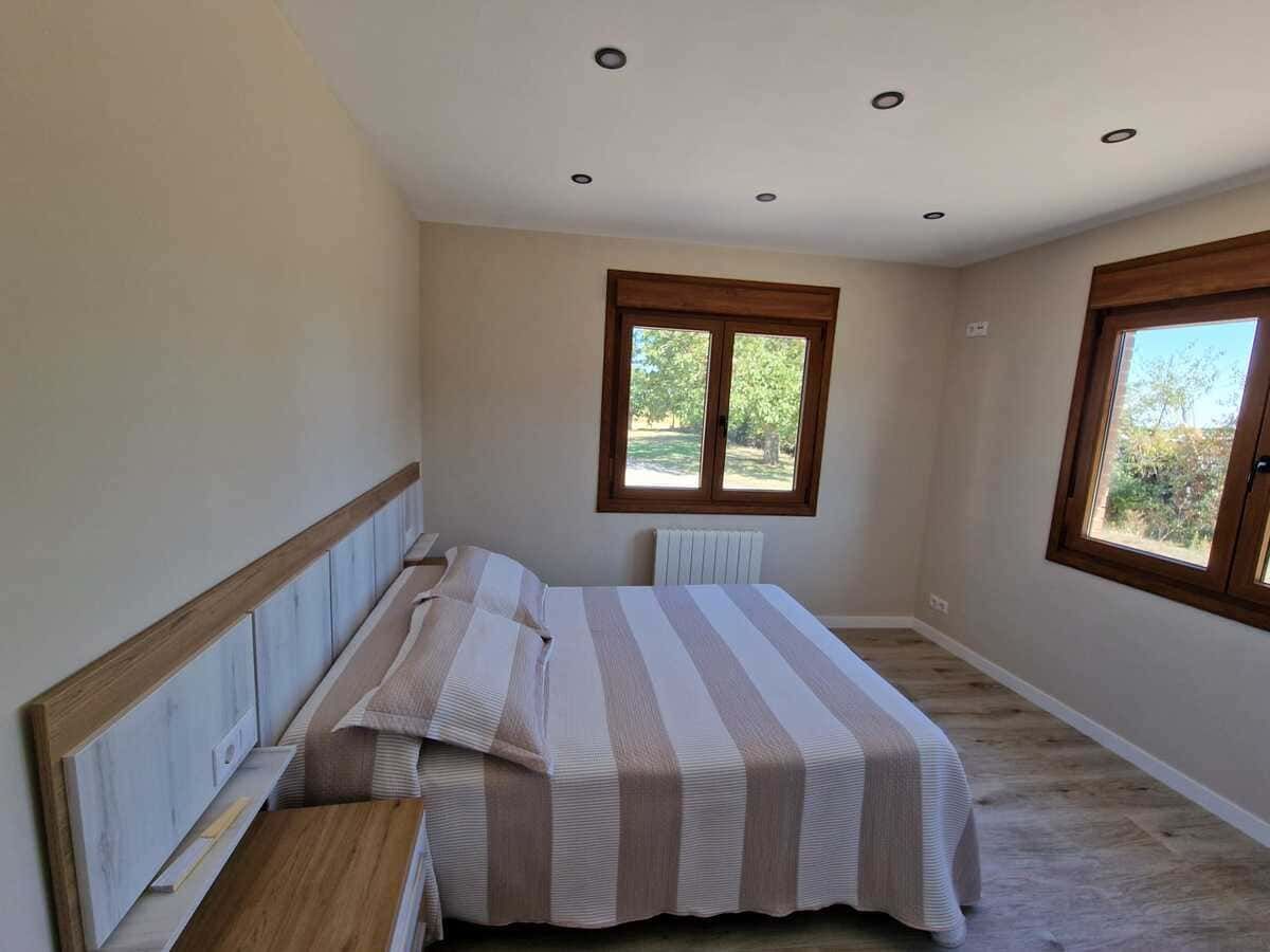 Dormitorio luminoso con colcha a rayas, ventanas con marcos de madera y luces empotradas en el techo.