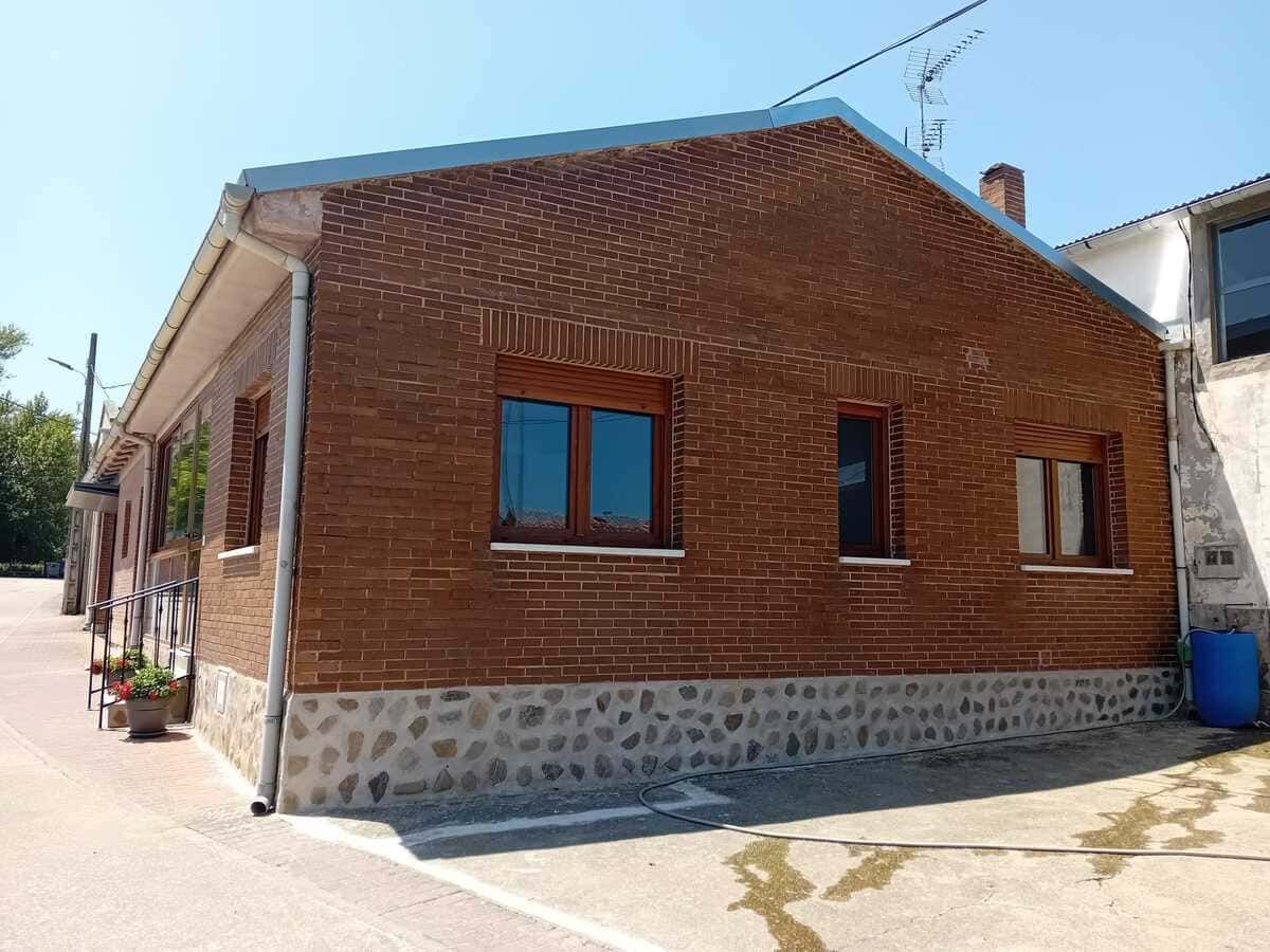 Patio soleado con mesa de madera, flores en macetas, parrilla de piedra y vistas a las montañas al fondo