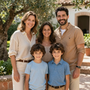 Familia de cinco personas sonriendo al aire libre en un jardín soleado, con dos niños delante y dos adultos detrás.