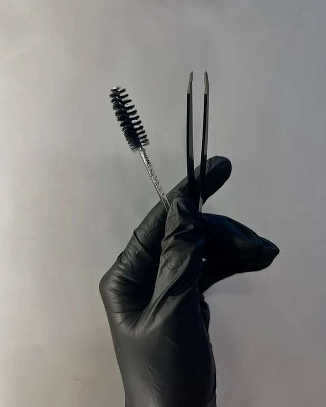 Una persona que lleva guantes negros sostiene un par de pinzas y un cepillo.