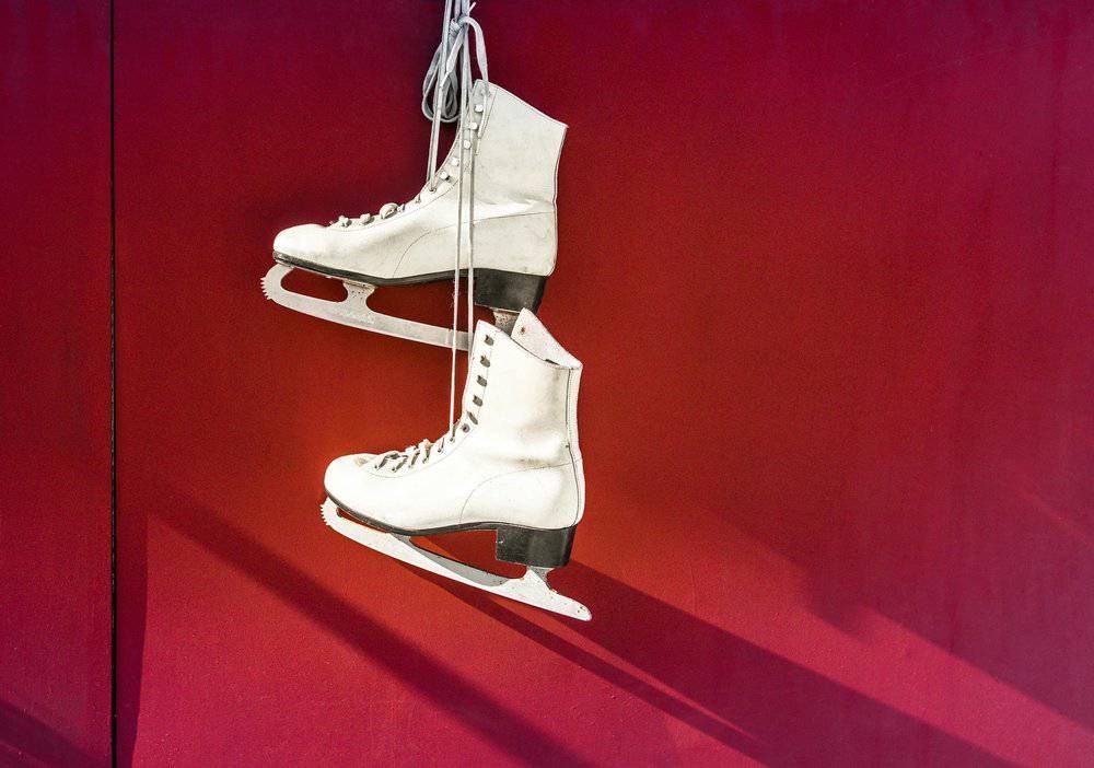 A pair of white ice skates hanging on a red wall.