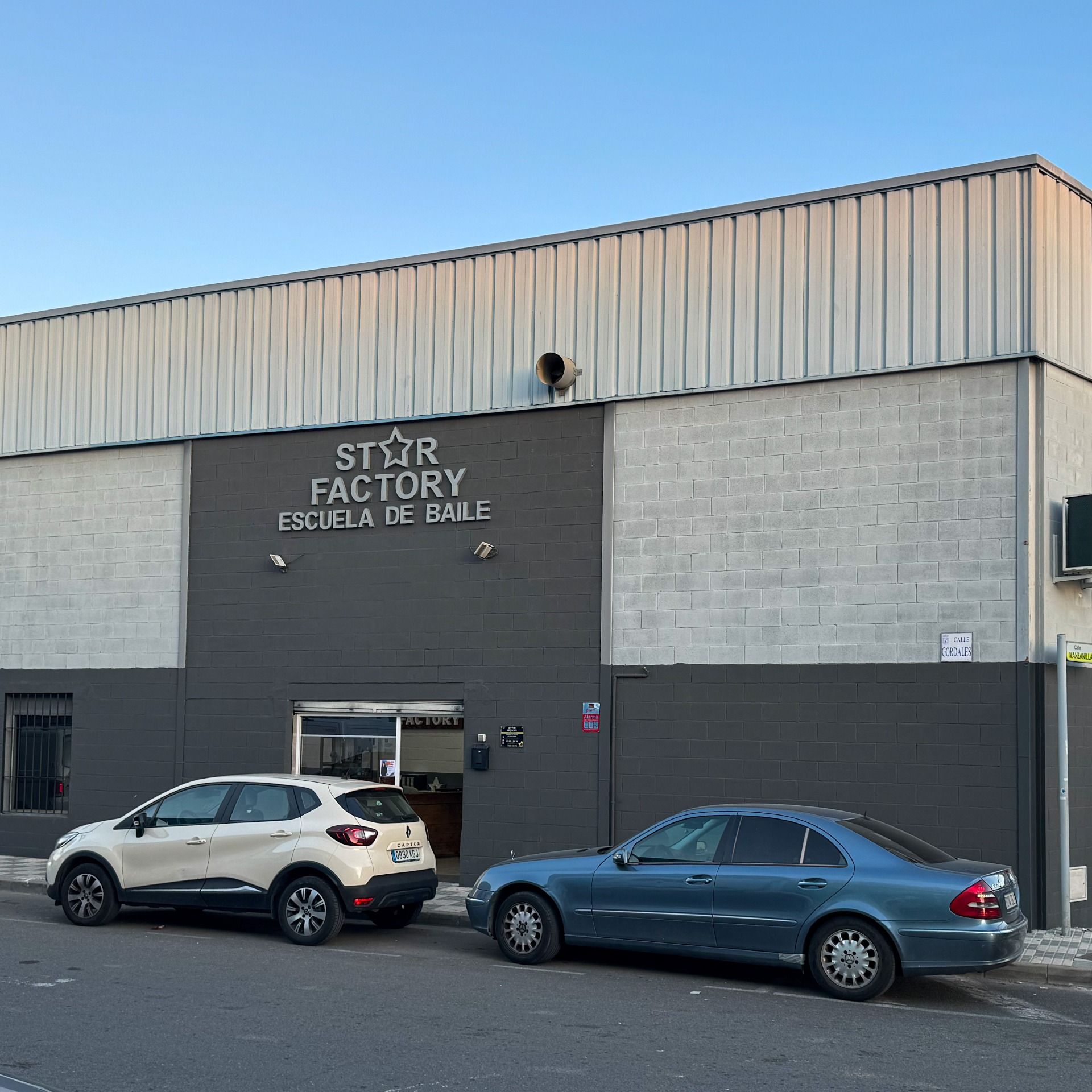 Dos coches están aparcados delante de un edificio que dice Fábrica de Estrellas.
