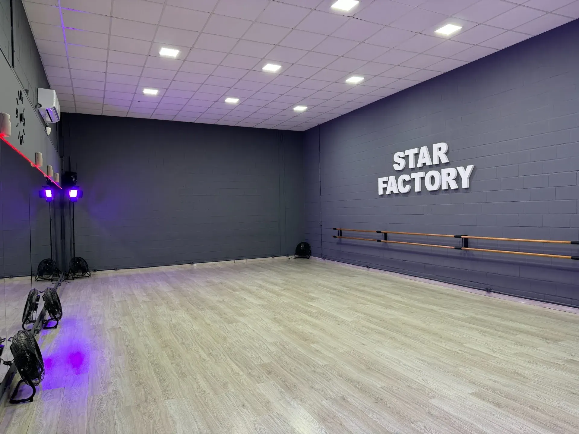 Un gran estudio de baile vacío con suelo de madera y luces violetas.