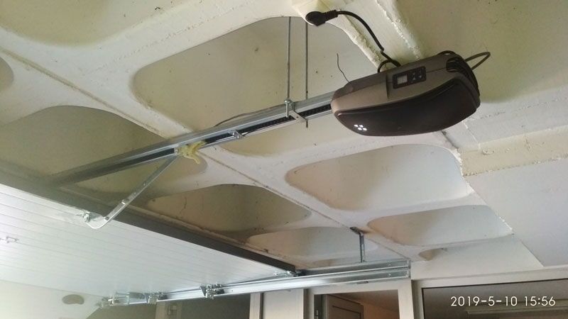 Abridor de porta de garagem montado em um teto branco texturizado com trilho de metal.