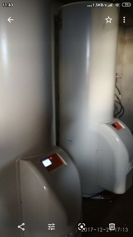 Dois aquecedores de água altos e brancos com painéis de controle em uma sala escura.