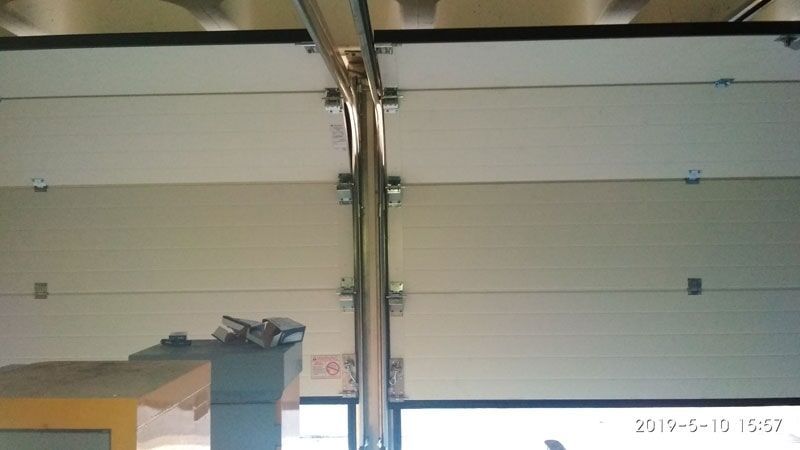 Uma porta de garagem com trilho torto e ferragens de conexão.