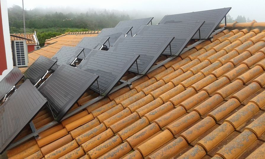 Painéis solares inclinados em um telhado de telhas. Os painéis são pretos e as telhas, laranjas. Fundo enevoado.