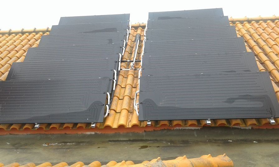 Painéis solares instalados em um telhado de telhas laranja. Os painéis são pretos e o céu está nublado.