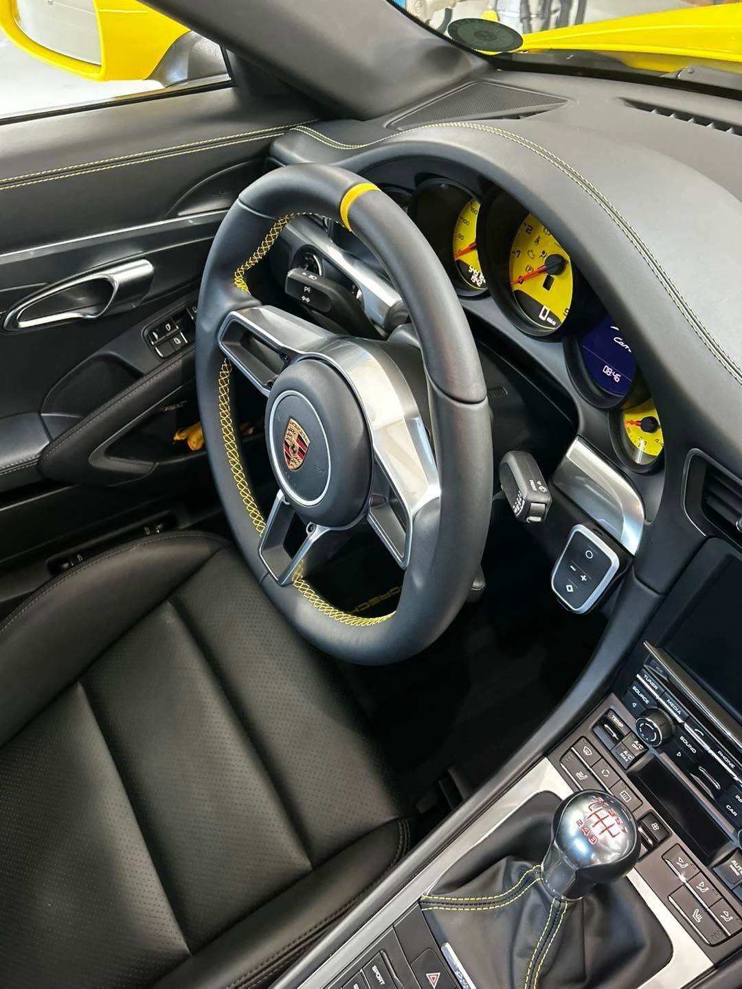 Porsche-Sportwagen-Interieur mit schwarzen Ledersitzen, gelben Akzenten an den Instrumenten und einem manuellen Schalthebel