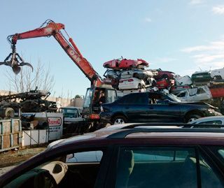 Un coche está aparcado delante de una pila de coches chatarra.
