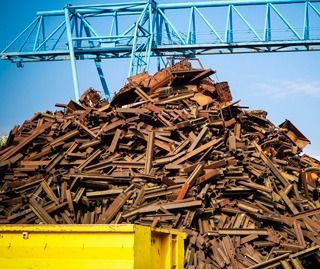Una gran pila de chatarra se encuentra encima de un contenedor de basura amarillo.