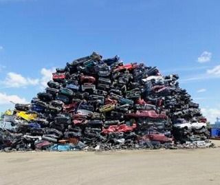 Una gran pila de autos chatarra se encuentra encima de un campo de tierra.