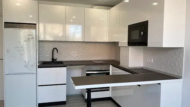 Cocina blanca moderna con encimeras, electrodomésticos y accesorios negros.