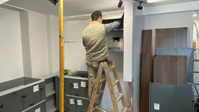 Un trabajador en una escalera instala estantes dentro de una habitación con gabinetes y suministros nuevos.