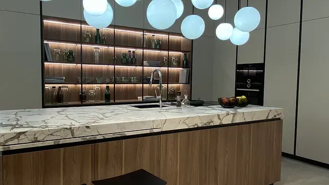 Cocina moderna con isla de mármol, gabinetes de madera, estantes retroiluminados con cristalería y luces de burbujas.