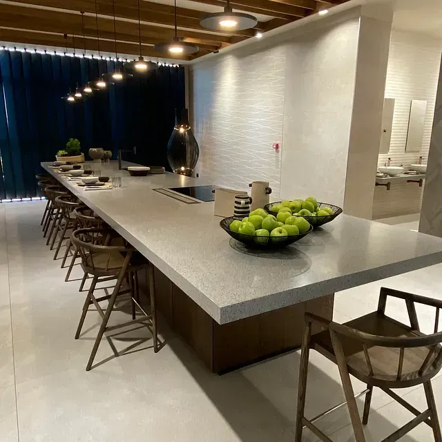 Una encimera larga y gris con taburetes y fruta. Iluminación superior en un espacio moderno y luminoso.
