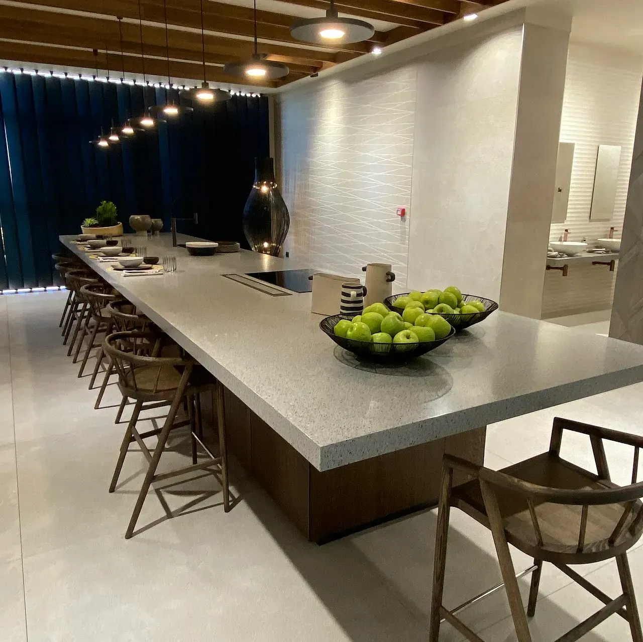 Mostrador rectangular largo con taburetes de bar, manzanas verdes y luces en el techo.