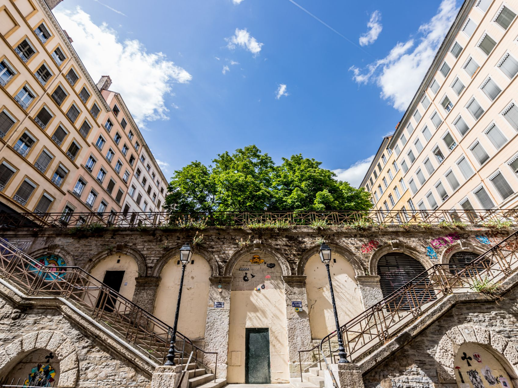 Un escalier en pierre monte entre deux grands bâtiments clair.