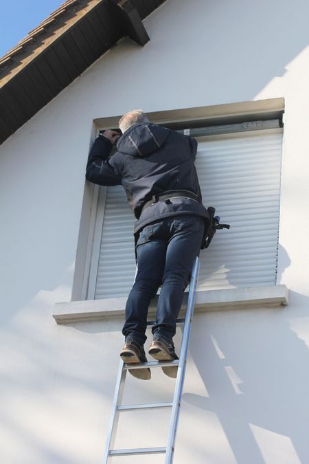 Ouvrier monté sur une échelle et réparant un volet