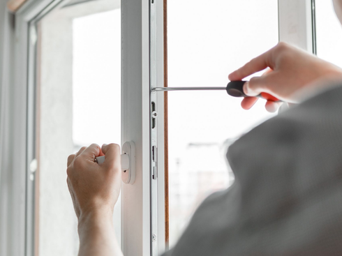 Une personne utilise un tournevis pour réparer les ferrures métalliques du cadre d'une fenêtre.
