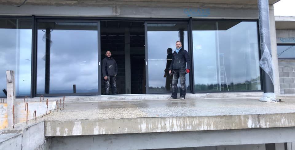 Deux personnes se tiennent devant de grandes portes coulissantes en verre sur un chantier de construction.