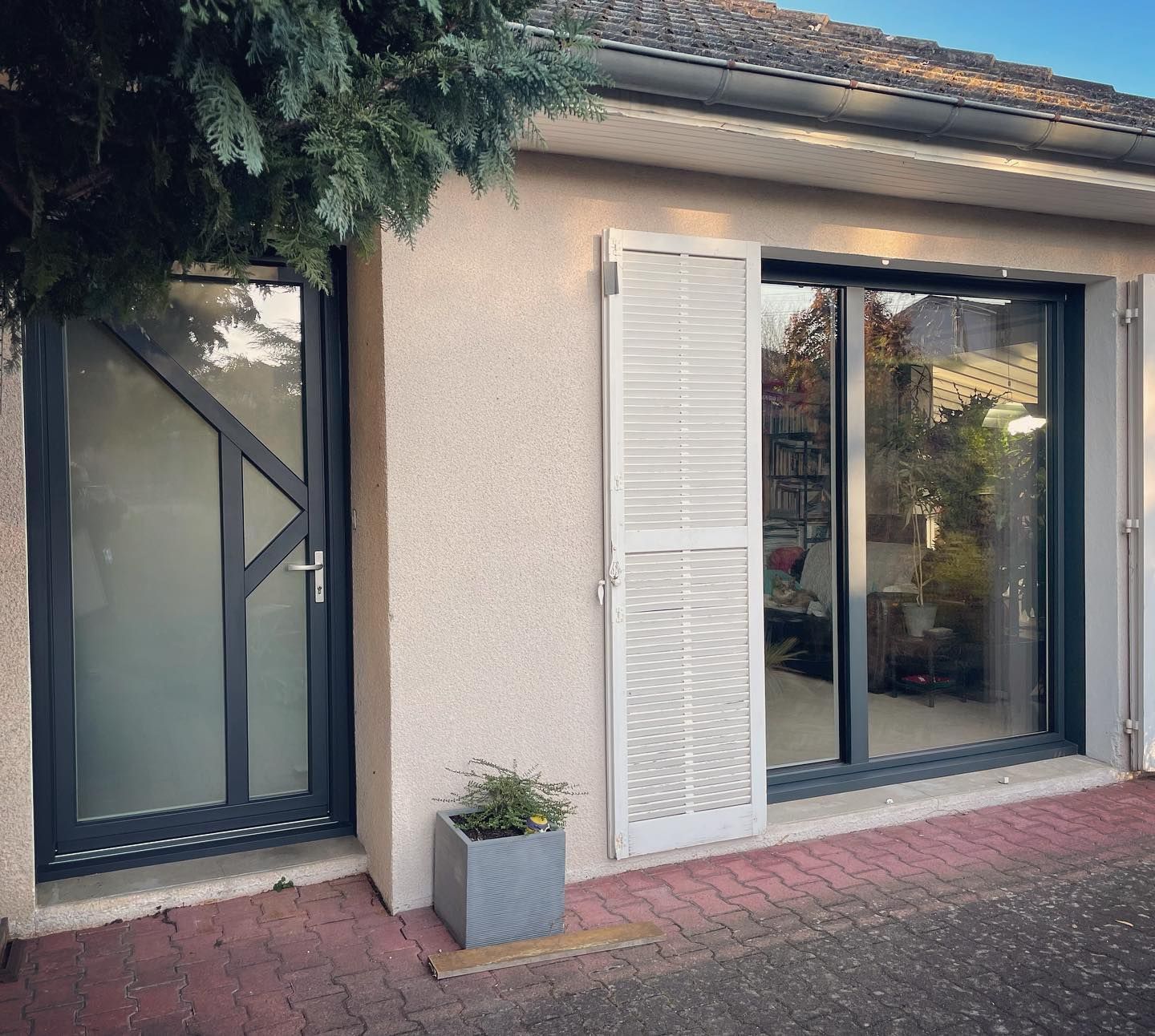 Vue extérieure d'une maison avec une porte gris foncé ornée de panneaux de verre géométriques, jouxtant une porte coulissante en verre assortie.