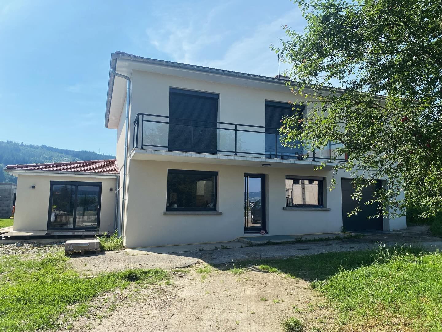 Une maison blanche de deux étages avec des volets foncés.