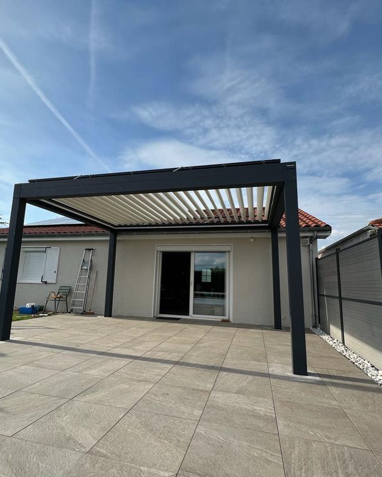 Une pergola moderne à structure noire et à persiennes blanches réglables.