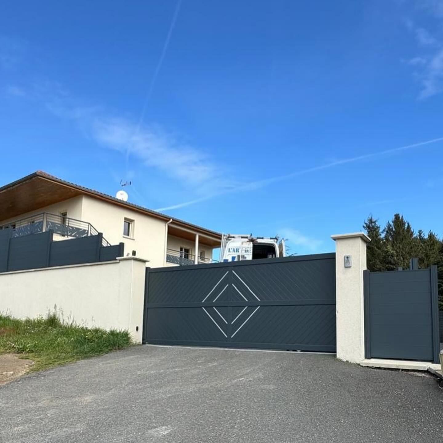Un portail coulissant moderne gris foncé, orné d'un motif géométrique en losange.