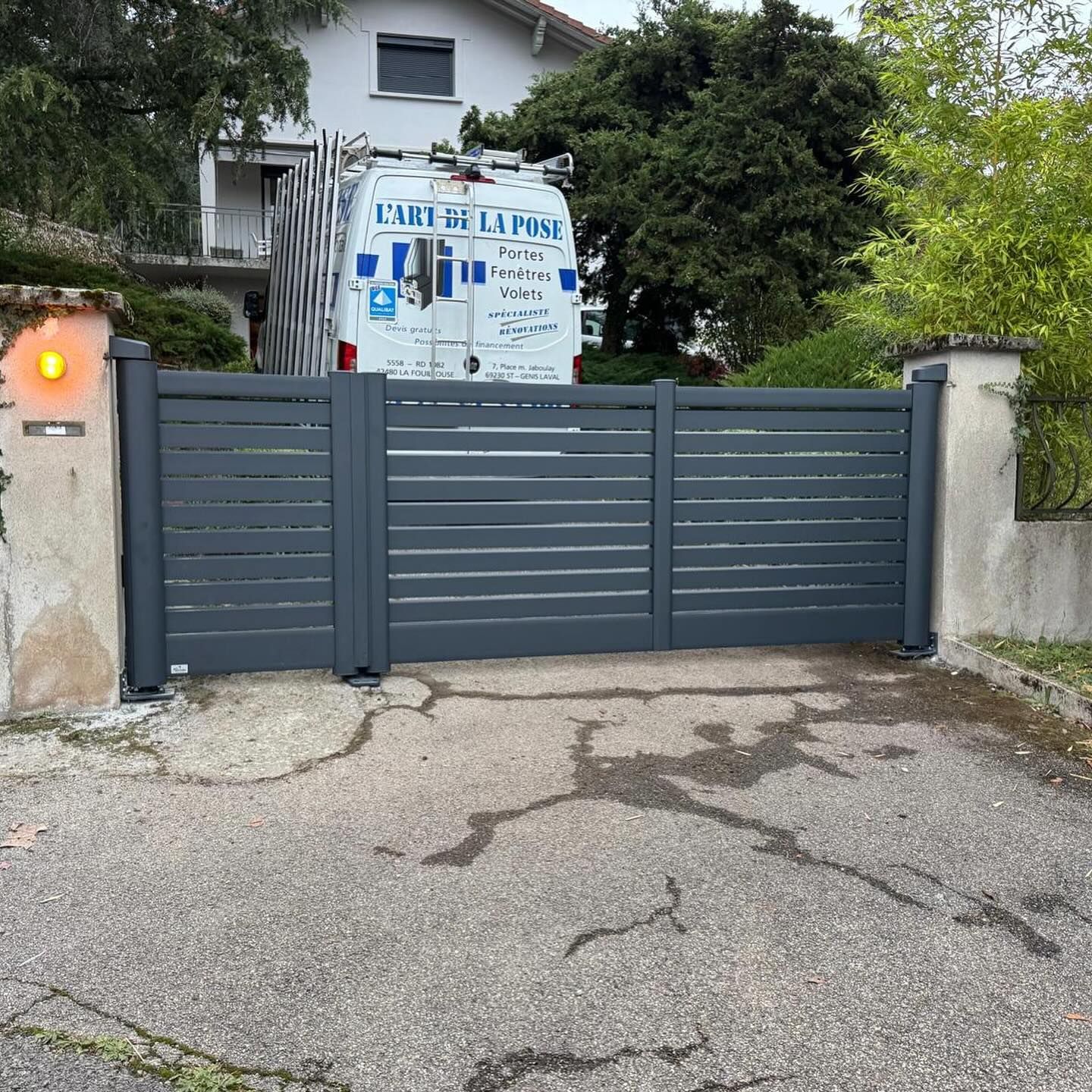 Un portail coulissant moderne à lames horizontales gris foncé est fermé.
