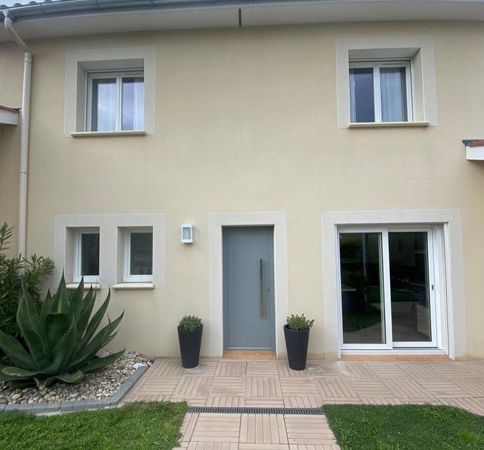Façade d'une maison moderne avec une porte d'entrée grise et des fenêtres à cadre blanc.