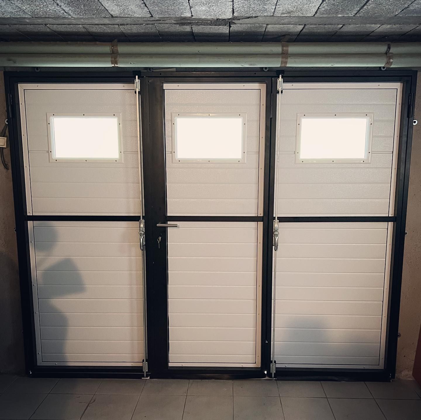 Trois panneaux de porte de garage blancs, avec des fenêtres rectangulaires et des cadres en métal noir.